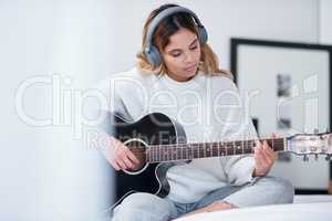 Allow your passion to become your purpose. a young woman wearing headphones while playing the guitar at home.