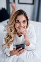 Social media is the easiest way to connect with one another. a young woman using her cellphone while lying on her bed.