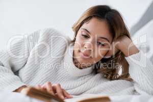 When you have some free time, read. a young woman reading a book while lying on her bed.