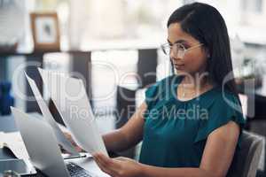 Managing her success with determination. a young businesswoman going through paperwork while working in an office.