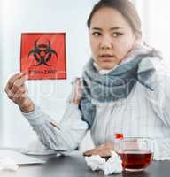 You can never be too safe. a young businesswoman holding a biohazard sign at her desk in a modern office.