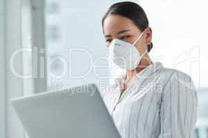 A good connection keeps you going through this crisis. a masked young businesswoman using a laptop in a modern office.