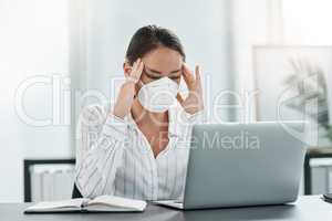 Struggling to find the strength to power through. a masked young businesswoman looking stressed while working at her desk in a modern office.