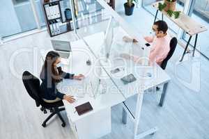 Screen partitions assist in creating work distancing. High angle shot of two businesspeople wearing face masks while working in an office.