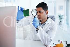 The most respected technician in the field. a young man using a magnifying glass while repairing computer hardware in a laboratory.