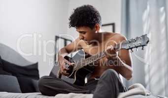 Good music makes your heart beat along with it. a young man playing the guitar in his bedroom at home.