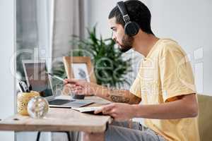Staying in place, keeping up the business pace. a young man using a laptop and headphones while working from home.