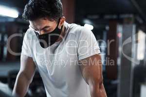 Working up a sweat, safely. a handsome and athletic young man wearing a mask while working out in the gym.