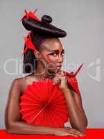 Cross cultural couture. Studio shot of a beautiful young woman wearing Asian inspired makeup and posing with a fan against a grey background.