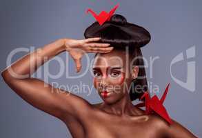 Theres beauty across all cultures. Studio shot of a beautiful young woman wearing Asian inspired makeup and posing with origami against a grey background.