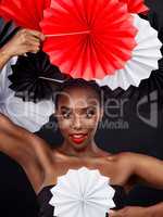 Weaving different cultures into one glorious look. Studio shot of a beautiful young woman posing with a origami fans against a black background.
