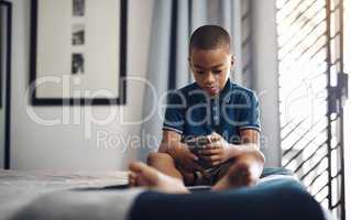 He only has access to content for 10 years and younger. a young boy using a cellphone while sitting on his bed.