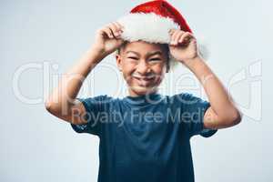 Reporting for Christmas elf duty. Studio shot of a cute little boy wearing a Santa hat against a grey background.