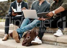 Whatever our location, lets get it done. a group of businessmen sitting on stairs and using a laptop during a meeting against a city background.