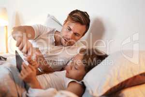 Bedtime stories are a lot more fun with e-books. a young boy using a digital tablet while lying in bed with his father.