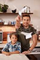 Lets see how high our planes can go. a man and his young son playing with paper planes at home.