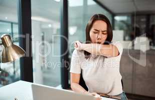 Practice good cough etiquette for the sake of everyones health. a young businesswoman coughing into her elbow in an office.