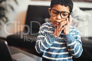 When technology turns into modern toys. an adorable little boy talking on a cellphone while using a laptop at home.