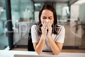 Dealing with a stuffy and runny nose. a young businesswoman blowing her nose while working in an office.