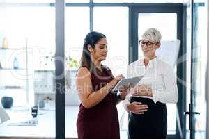 Finding solutions that will drive success into their business. two businesswomen using a digital tablet together in an office.