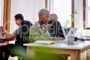 Ill send a voice memo to the client. a young businesswoman using a cellphone and laptop in an office.