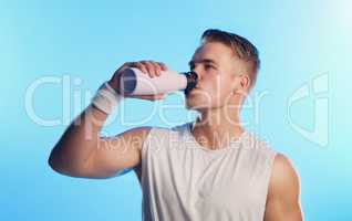 Staying hydrated throughout his workout. Studio shot of a handsome young man drinking from a water bottle against a blue background.