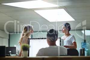 Young colleagues having a serious discussion at work in a modern office. Business women talking while colleague is working in the workplace. Females having an informal meeting at the office.