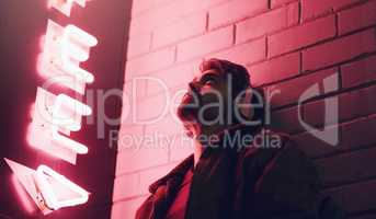 Put on your headphones and forget everything else. a young man wearing headphones while leaning against a building at nighttime.