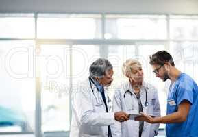 Medical professional, team and workers holding tablet, talking and solving a problem together online while standing at work in a hospital. Health experts discussing, planning and doing research