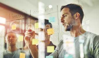 Confident, smart and creative team designing a strategy idea and writing on sticky notes on a transparent glass board. Group using teamwork, planning and collaboration in a brainstorming meeting