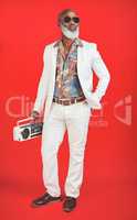 People hear me coming before they see me. Studio shot of a senior man wearing vintage clothing while posing with a boombox against a red background.
