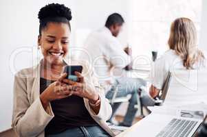 Responding to my text messages. an attractive young businesswoman sitting in her office with her coworkers and using her cellphone.