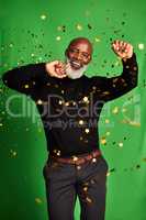 Everyday should be celebrated. a senior man dancing while confetti falls over him against a green background.