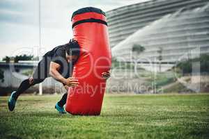 Train today, win tomorrow. Full length shot of a handsome young rugby player working out with a tackle bag on the playing field.