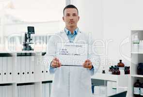 Seek help if you see any of these symptoms. Portrait of a young scientist holding a sign with a list of COVID-19 symptoms on it in a modern laboratory.