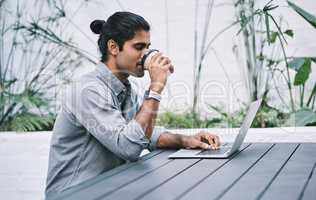 Coffee keeps those numbers up. a young businessman using a laptop and having coffee in a modern workplace.