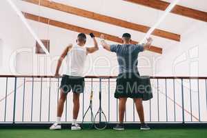 Whats sport without its fans. Rearview shot of two young men cheering while watching a game of squash from the viewing gallery.