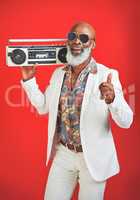 Music is what uplifts the spirit. Studio shot of a senior man wearing vintage clothing while posing with a boombox against a red background.