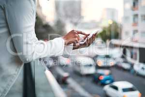 Businessperson texting on their mobile phone to send an email outside on the balcony of a modern office, overlooking a busy city. Corporate professional worker typing outdoors to send a text message