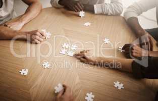 Friends hands solving a puzzle in a group collaboration together as a team on wooden table indoors. Diverse colleagues using teamwork and support to help each other to find a smart solution close up