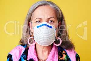 Protect your golden years at all costs. Portrait of a quirky senior woman wearing a N95 face mask against a yellow background.