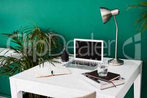 Take a seat and get busy. Still life shot of various items at a workstation against a green wall in an office.