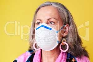 Stay protected and hopeful for the years ahead. a quirky senior woman wearing a N95 face mask against a yellow background.