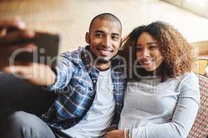 Smile babe. Happy, romantic and in love couple taking a selfie together on phone sitting on couch. Smiling young spouses hugging while holding phone to take a picture in the living room.