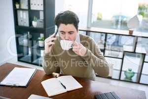 Fuelling up for a busy and productive day. a young businessman talking on a cellphone while drinking coffee in an office.