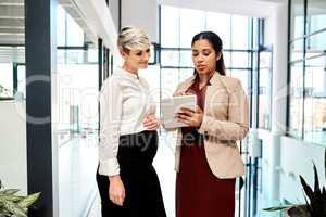 Collaboration is key in their industry. two businesswomen using a digital tablet together in an office.