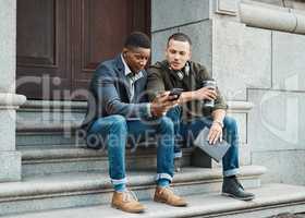 Business looks a lot more leisurely these days. two young businessmen using a smartphone together against an urban background.