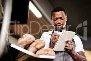 Now Im halfway through my order list. a male baker making notes while working in his bakery.