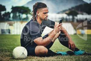 Im pretty sure my teammates should be here by now... Full length shot of a handsome young rugby player using a smartphone while sitting in the playing field during the day.
