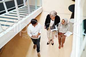 Heading off to their next meeting together. High angle shot of a group of businesspeople walking alongside each other in an office.